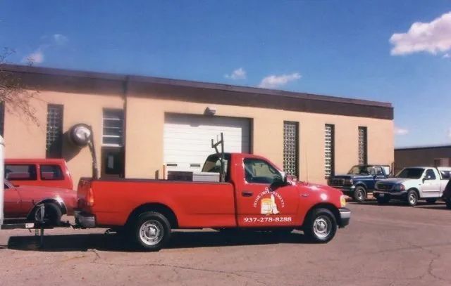 Red tow truck parked outside a beige garage under a blue sky.