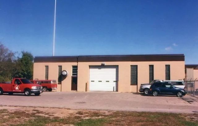 Two parked cars in front of a small beige building with a white garage door under a blue sky