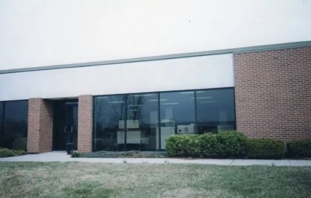 Office building with dark glass windows and brick walls, viewed across a grassy lawn