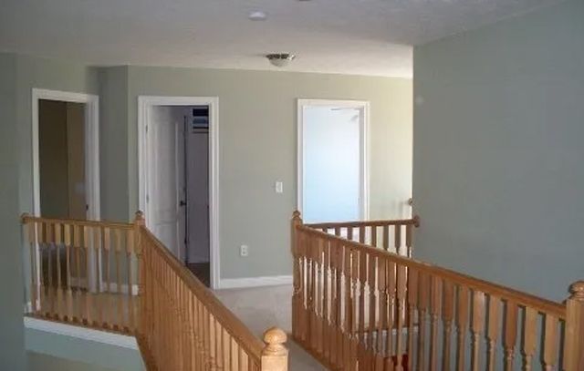 Empty upstairs hallway with wooden railings, beige walls, and open doorways