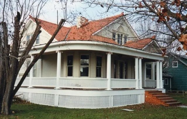 White house with wraparound porch, red roof, and bare trees in front