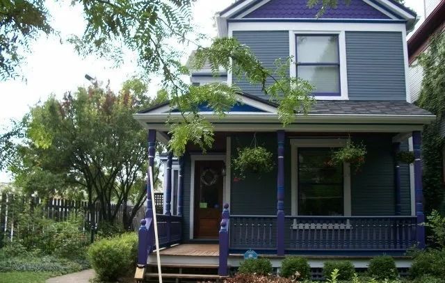 Blue two-story house with a front porch, white trim, and trees in the yard