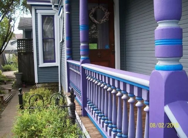 Purple porch railing beside a blue house with a small garden walkway