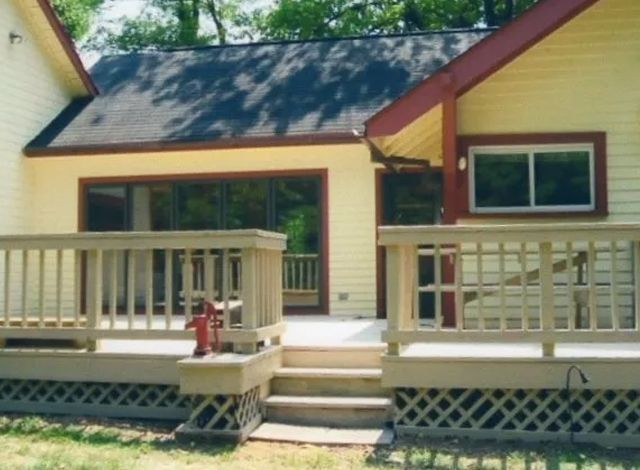 Yellow house with front porch, railing, steps, and lattice skirting under a dark roof.