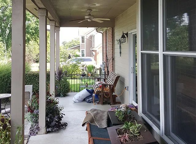 Covered front porch with potted plants, chairs, and a small table overlooking a garden walkway