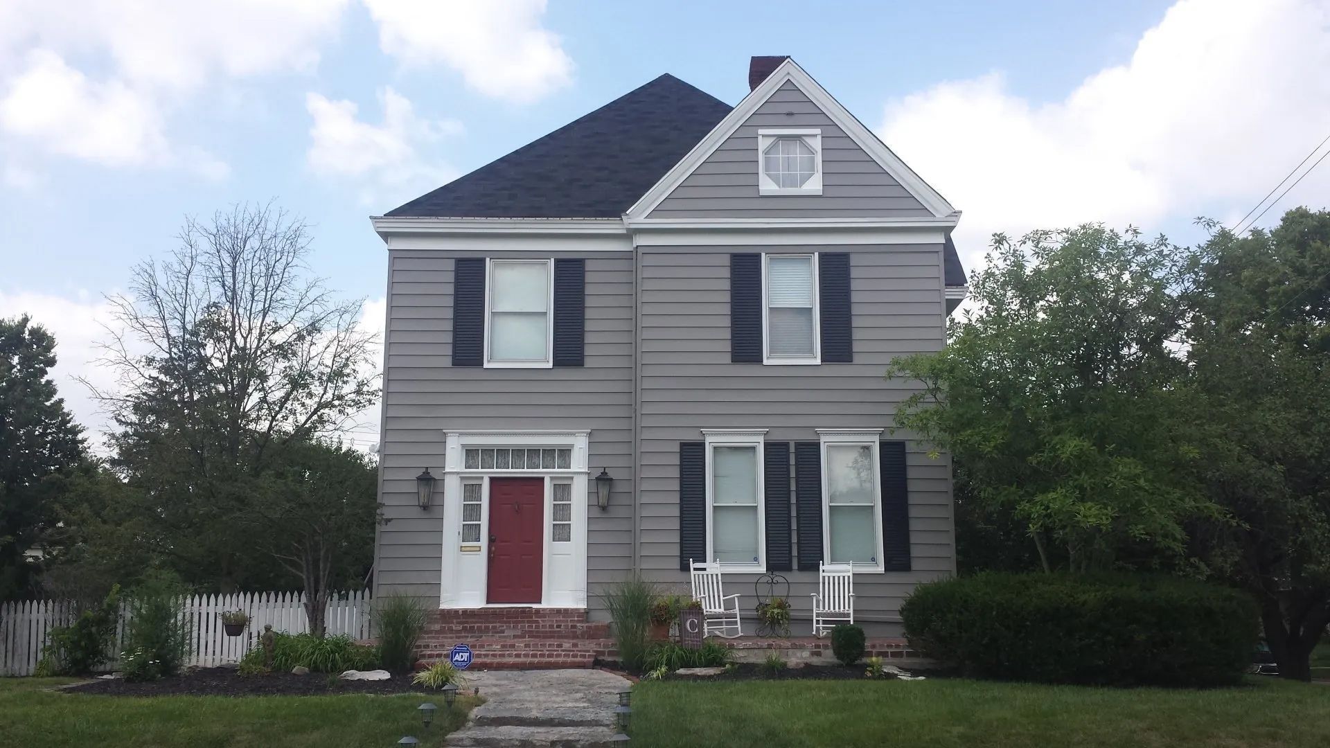 Two-story gray house with white trim, red front door, and a small front yard.
