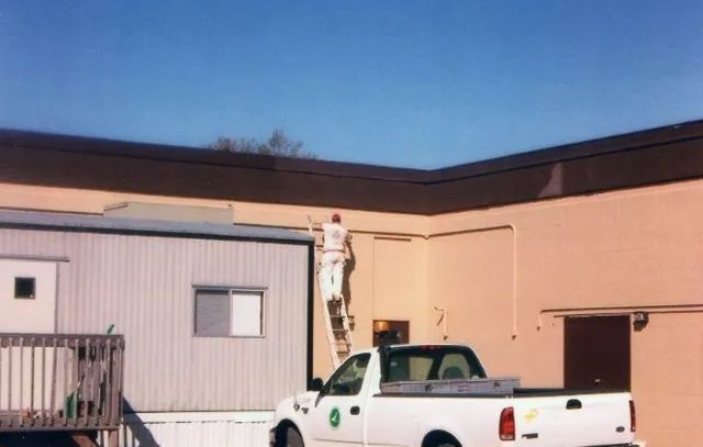 Person standing on a white pickup truck outside a beige building