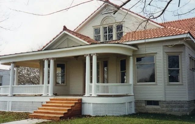 Front porch of a light gray house with white columns and orange steps