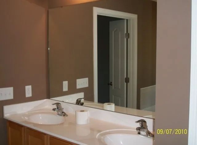 Bathroom vanity with double sinks, large mirror, and open doorway in a beige room