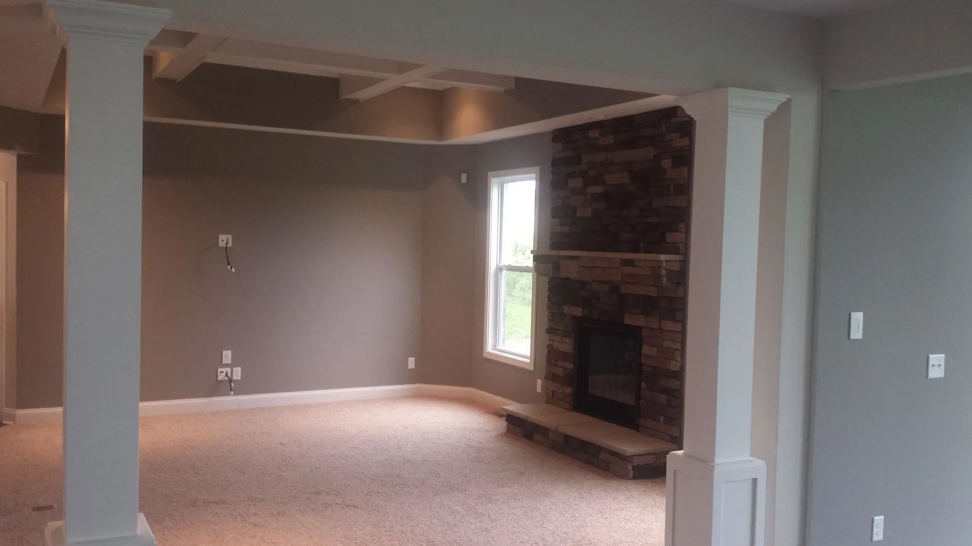 Empty living room with beige carpet, gray walls, and brick fireplace near a window