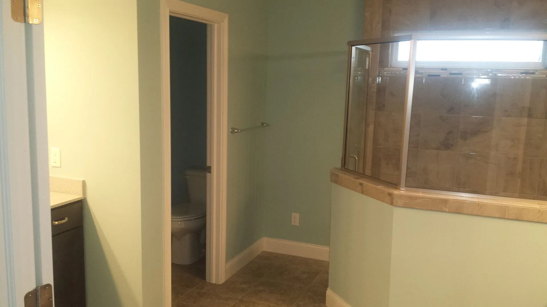 Bathroom with a glass-enclosed shower, open door to toilet, and beige tile flooring.