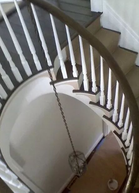 Spiral staircase with white balusters and a hanging chain chandelier over a lower floor.