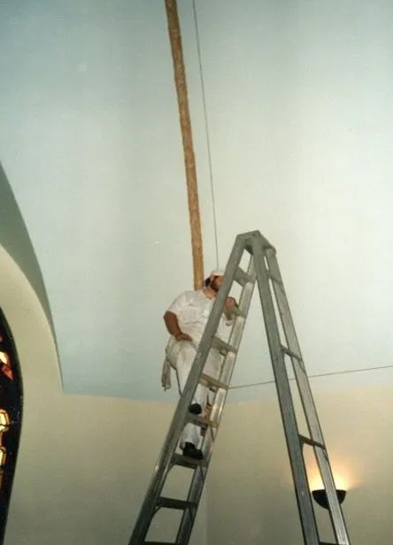 Person on a tall ladder painting a curved ceiling in a large room