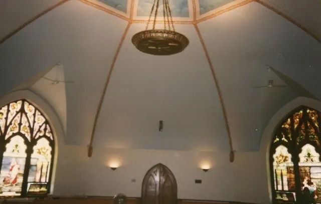 Interior of a vaulted chapel with stained-glass windows and a hanging chandelier under a domed ceiling