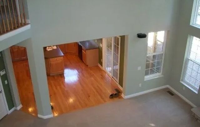 Spacious living room with beige carpet, hardwood entryway, and large windows looking into a kitchen.