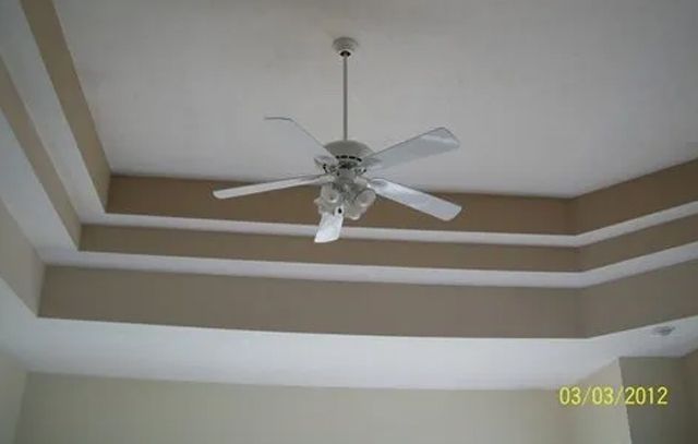 White ceiling fan hanging from a tray ceiling with beige trim in a room.