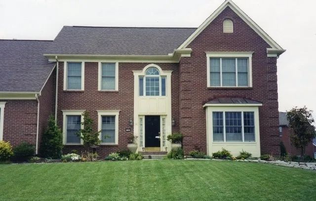 Brick suburban house with dark roof, white-trimmed windows, and a green front lawn