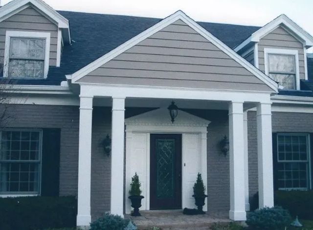 Front entrance of a gray house with white trim, columns, and a peaked porch roof.