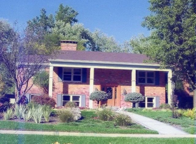 Brick house with white trim, front lawn, and walkway under trees on a sunny day