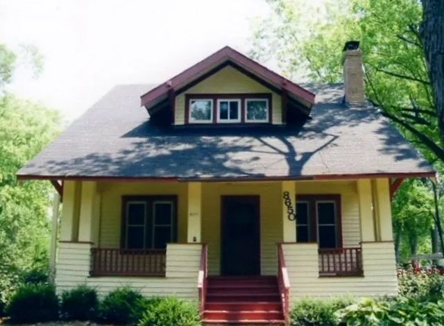 Yellow house with a red porch, dark roof, and front steps surrounded by trees