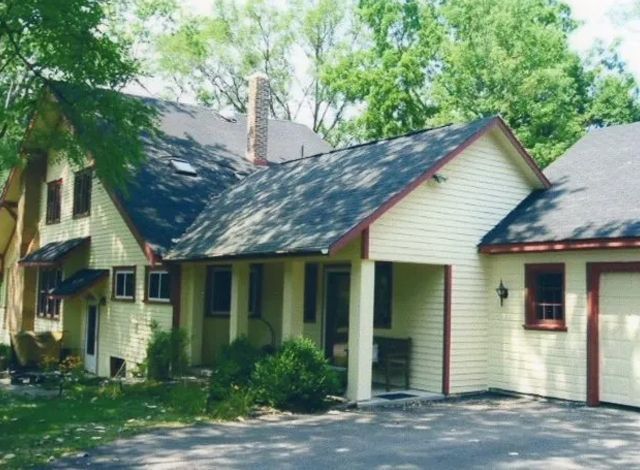 Yellow house with a red-trimmed roof and porch, surrounded by trees and greenery