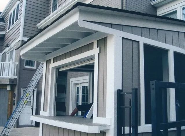 Partially built house exterior with gray siding, white trim, and a ladder leaning against it