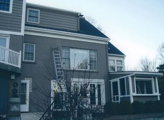 Gray two-story house with a ladder leaning against an upstairs window and a screened porch on the right