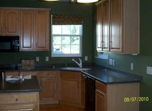 Kitchen with wood cabinets, dark countertops, green walls, and a window above the sink.