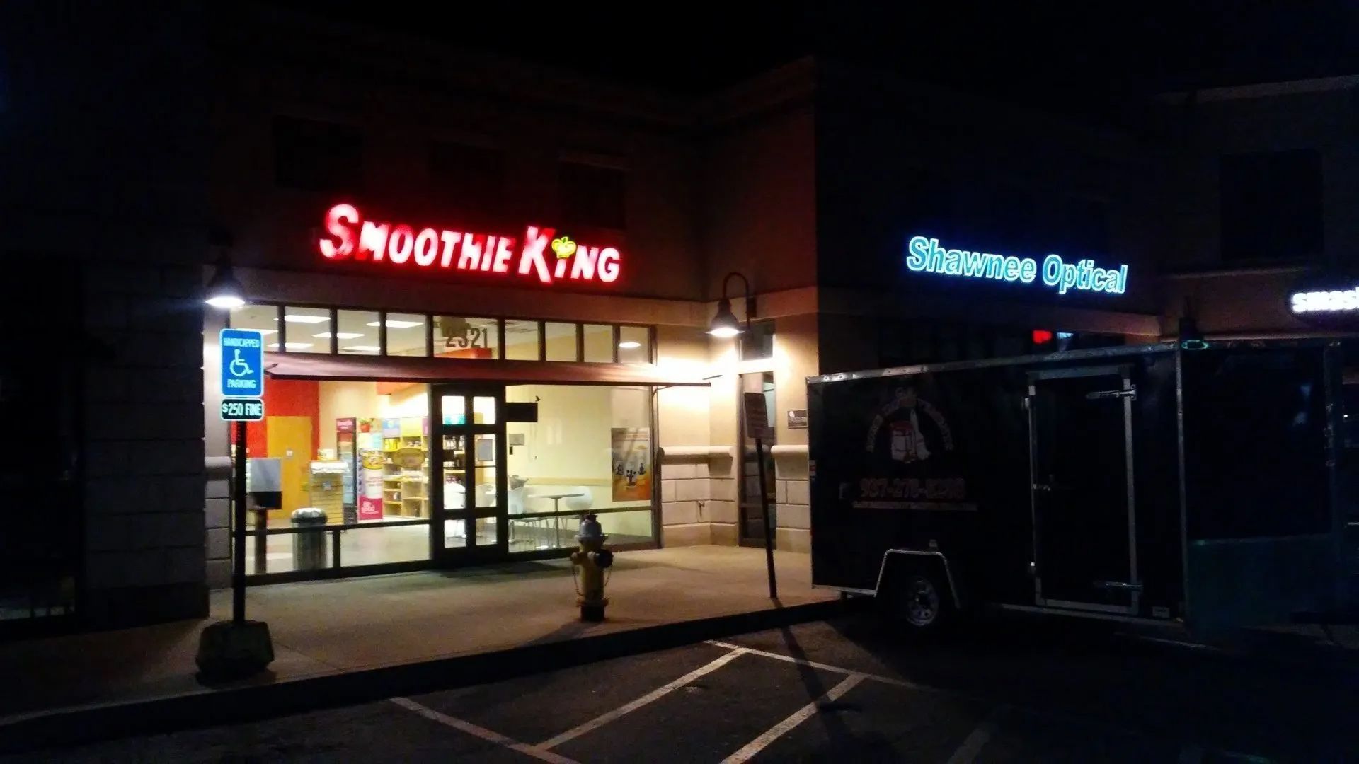 Nighttime exterior of a Smoothie King storefront with lit signs and a parked van in front.