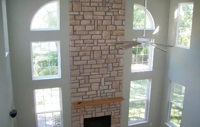 Tall living room with stone fireplace, arched windows, and a ceiling fan over white walls