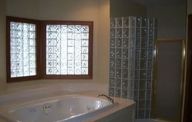 Bathroom with a white bathtub, glass block window, and tiled shower area