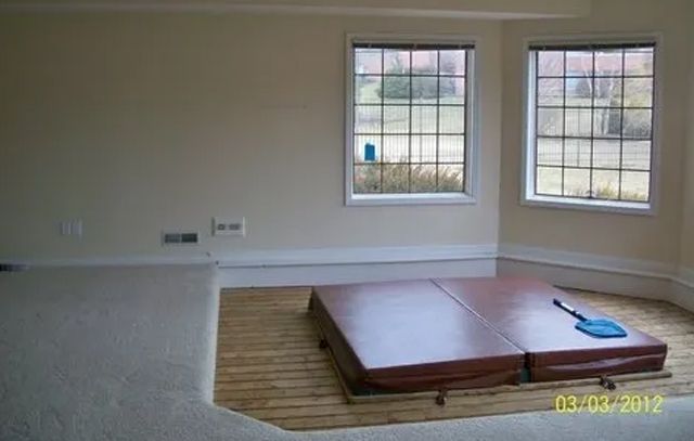 Living room with a recessed floor platform by two windows and a blue broom on carpeted floor