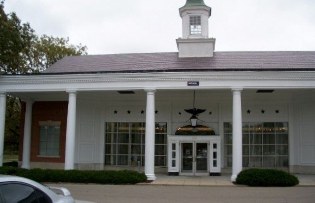 Front entrance of a white building with columns, a small cupola, and a central doorway under a bird emblem