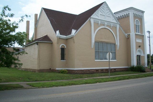 White church building with a tall steeple and arched windows beside a street