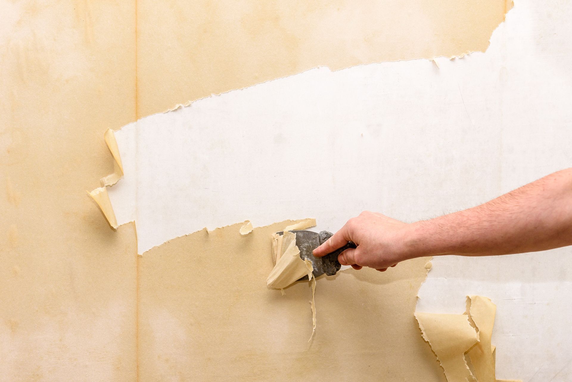 Hand scraping peeling beige paint off a wall, revealing white underlayer