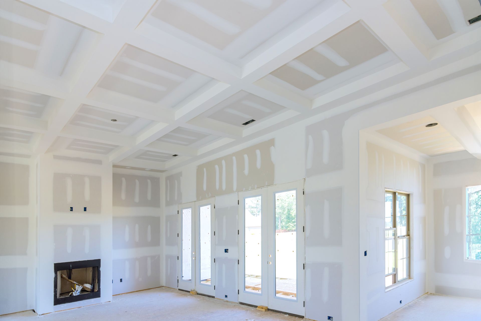 Bright unfinished white room with coffered ceiling, fireplace, and large windows/doors.