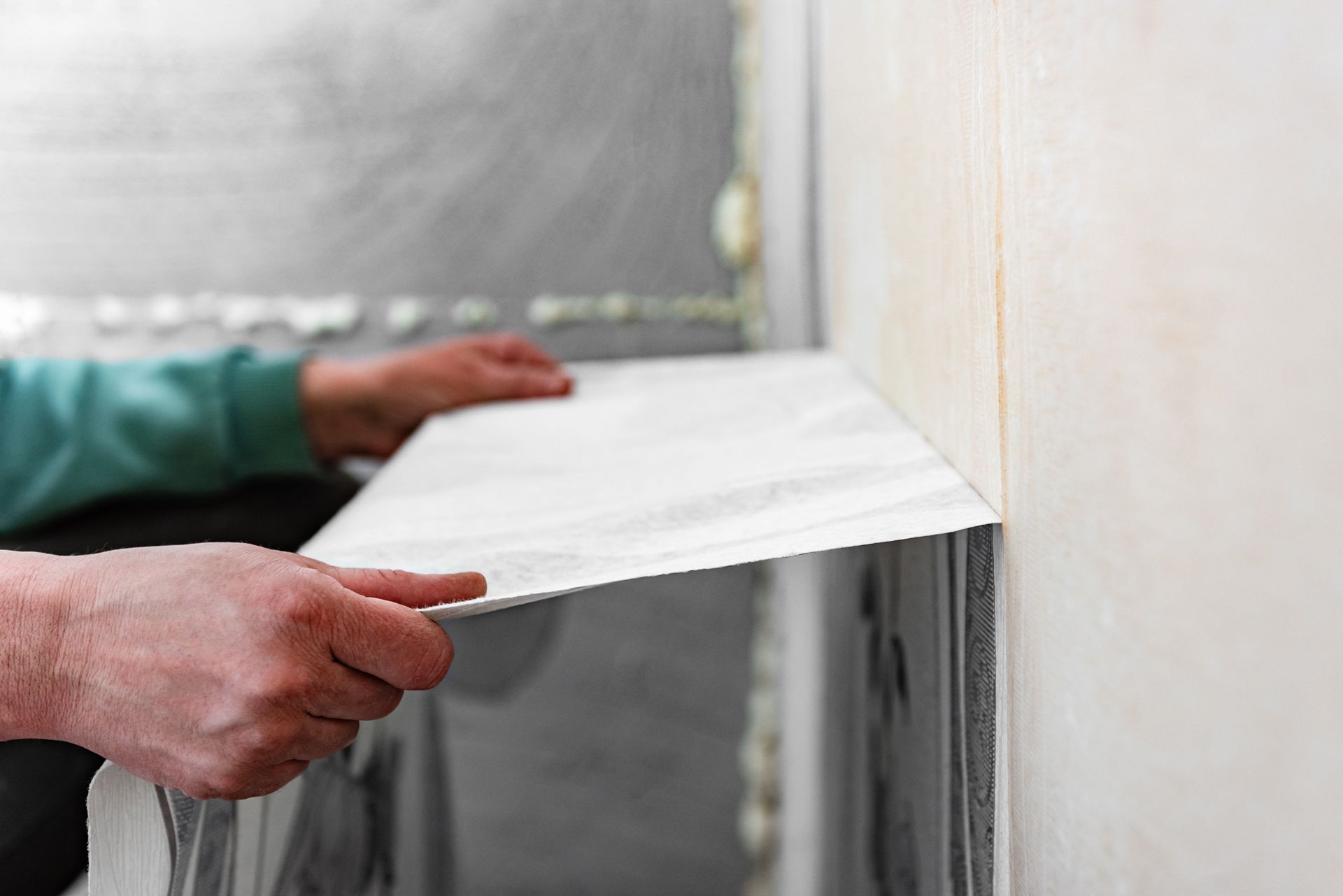 Hands installing white insulation board against an interior wall
