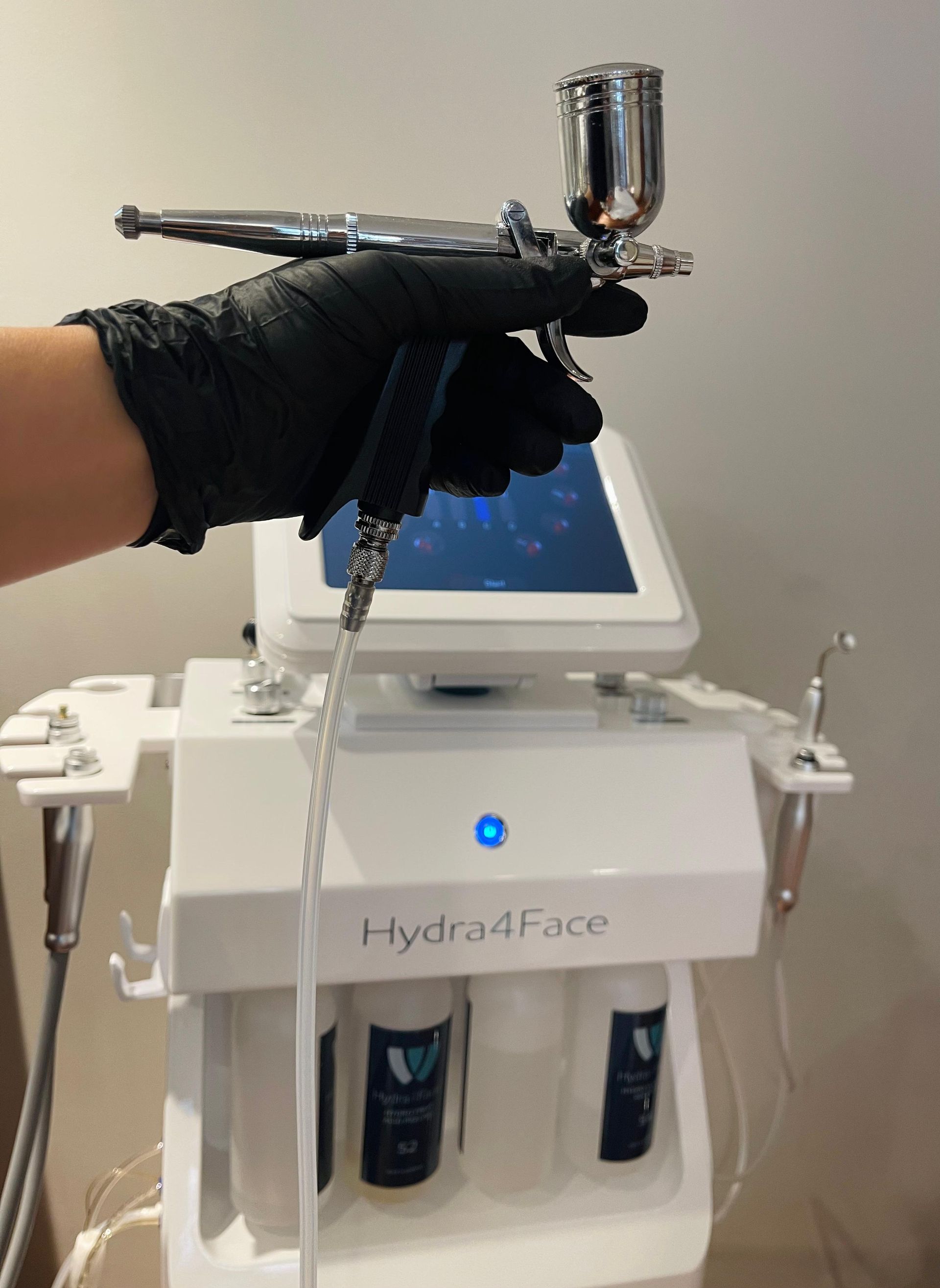 Eine behandschuhte Hand hält ein Hautbehandlungsspraygerät über einem Hydra4Face-Gesichtsbehandlungsgerät.