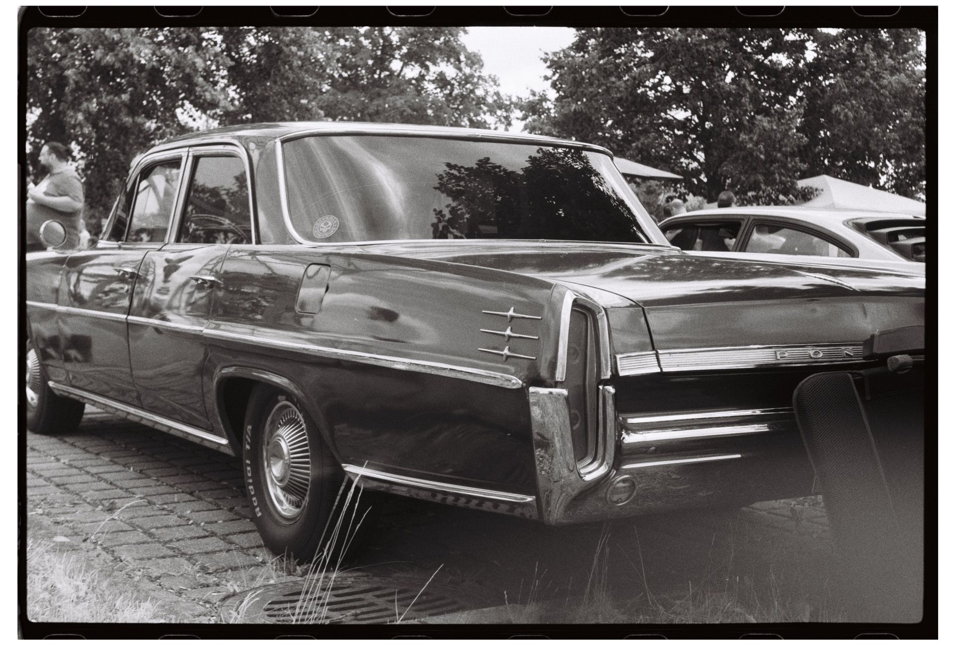 Black-and-white photo of a classic car parked outdoors, viewed from the rear side.