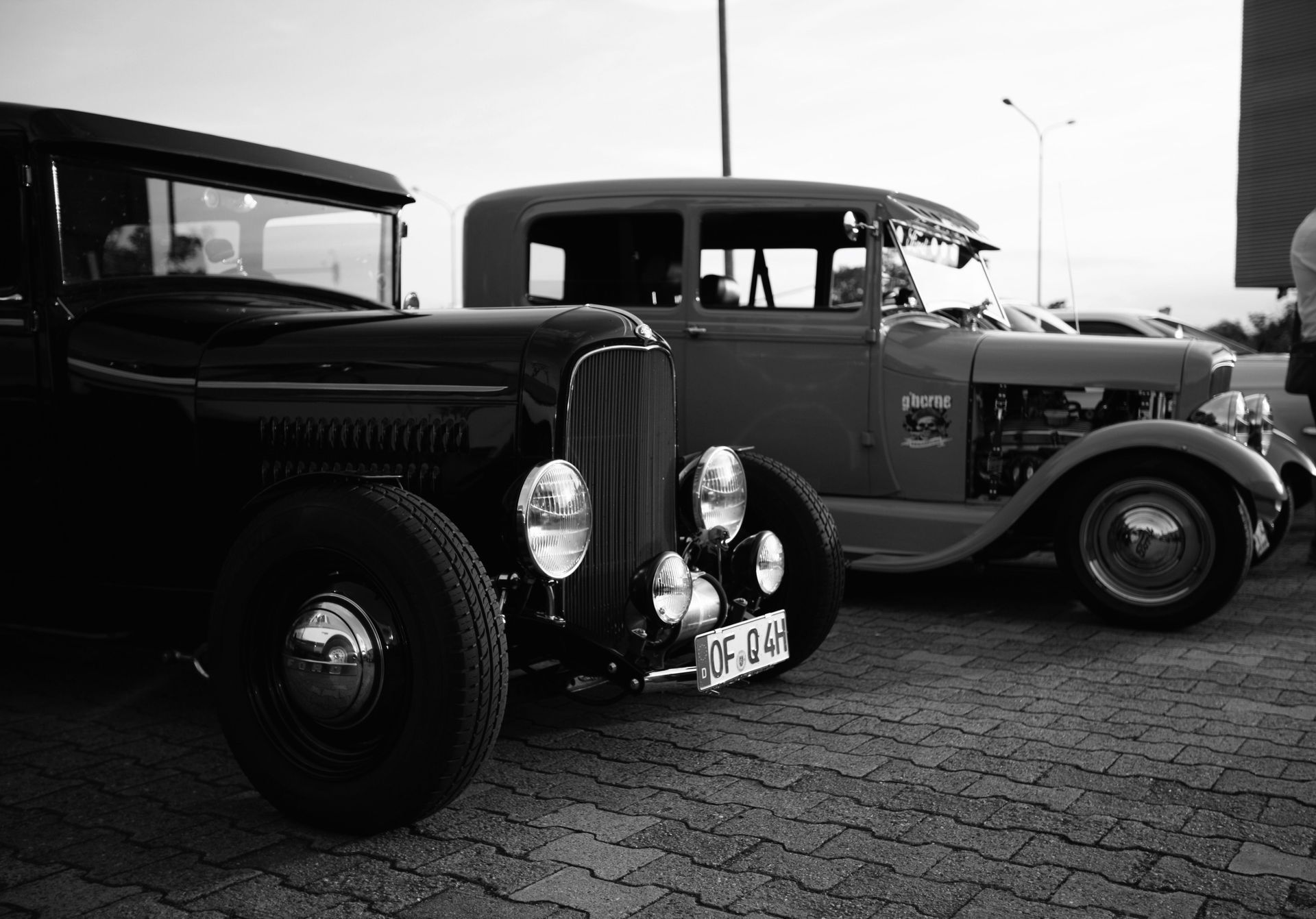 Two vintage cars parked side by side on a cobblestone street