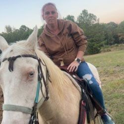 Woman on a palomino horse in field, wearing brown hoodie, jeans.