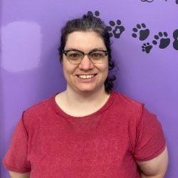 Woman with glasses in red shirt smiles in front of purple wall with paw prints.
