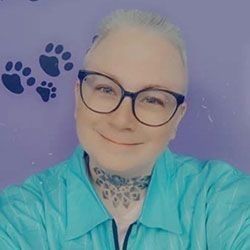 Smiling person with glasses, light skin, and a teal shirt against a purple background with paw prints.