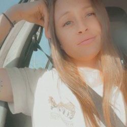 Woman with long blonde hair in a car smiles at the camera.