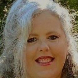 Woman with long gray hair smiles at the camera outdoors.