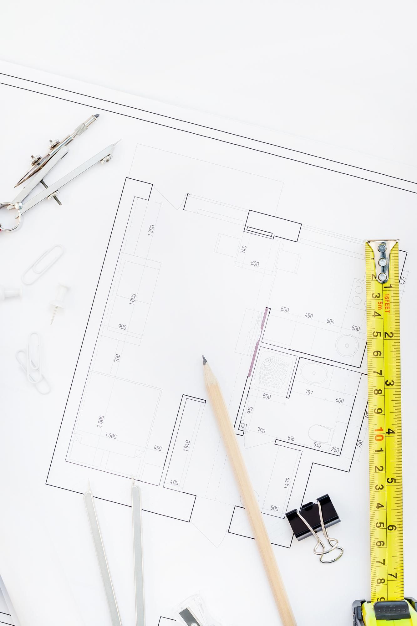 A drawing of a house with a tape measure , pencil , and compass on a table.