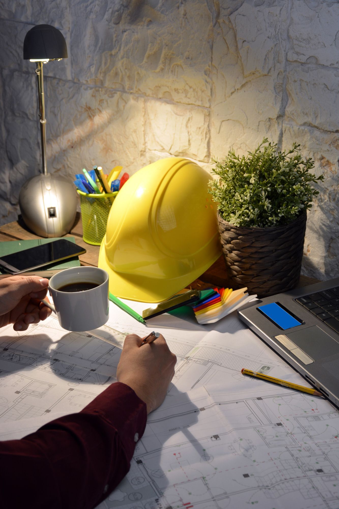 A person is sitting at a desk with a hard hat and a cup of coffee.