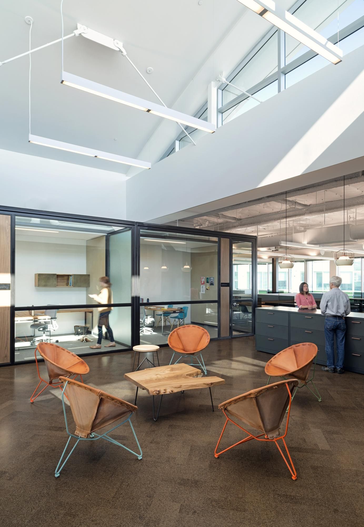 Modern office lounge with orange chairs, low tables, and people at a reception counter