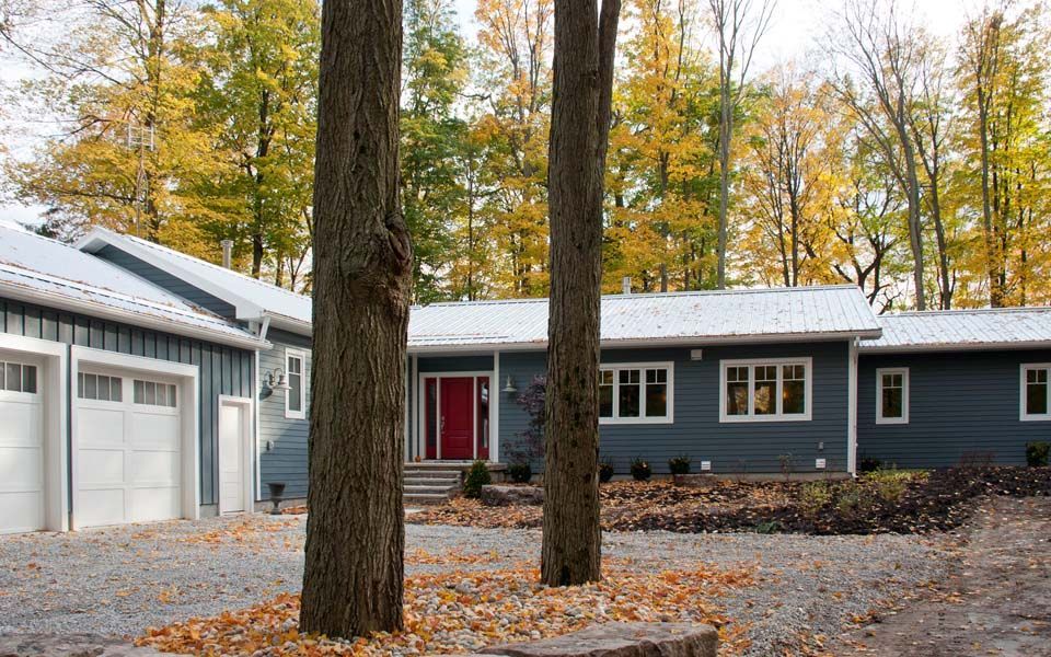 A blue house with a red door is surrounded by trees