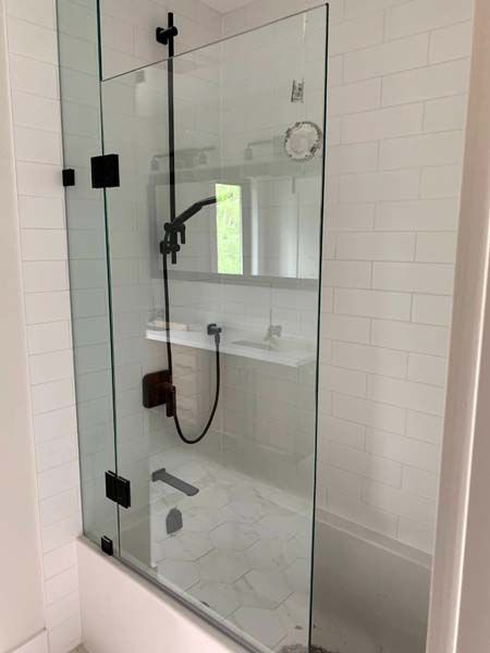 Glass shower enclosure with black hardware in a white-tiled bathroom